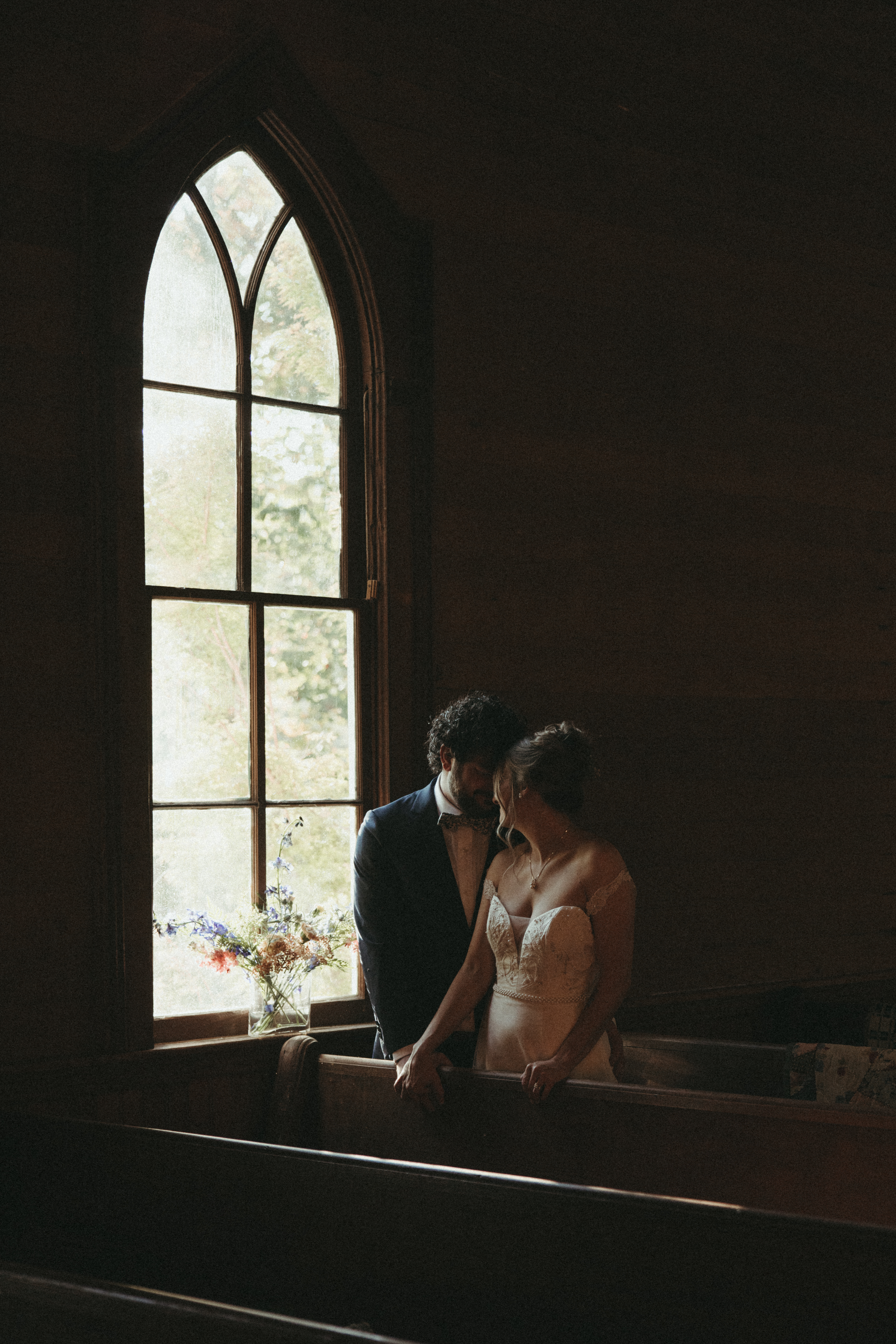 moody harsh light bride and groom portraits in a chapel in front of chapel windor
